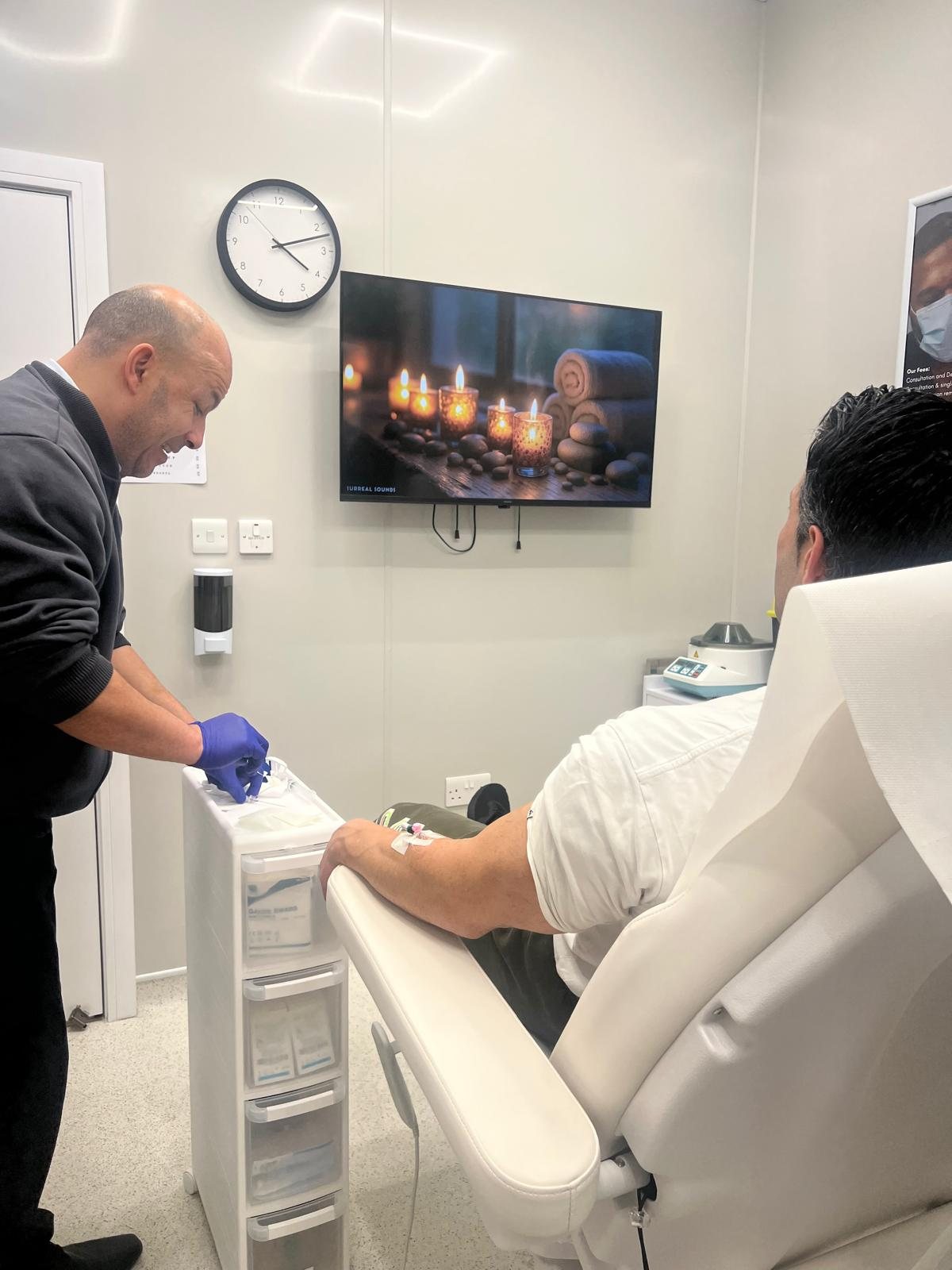 A clinician taking a blood sample from a patient in a treatment room