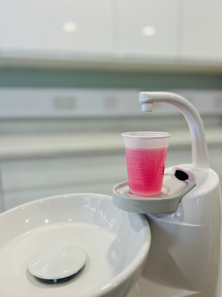 A cup of pink mouthwash on the rinse stand of a dental chair